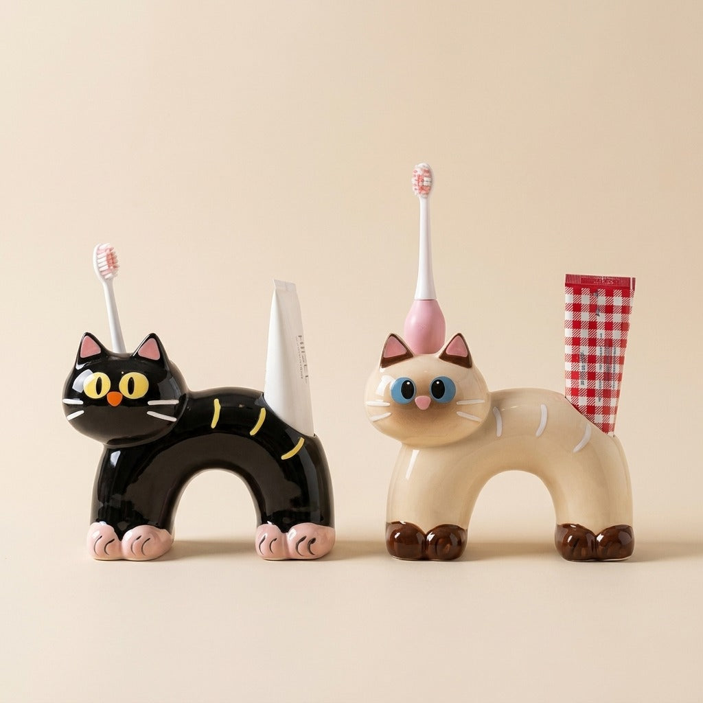 Two ceramic cat toothbrush and toothpaste holders in black and cream, sitting on a neutral tabletop.