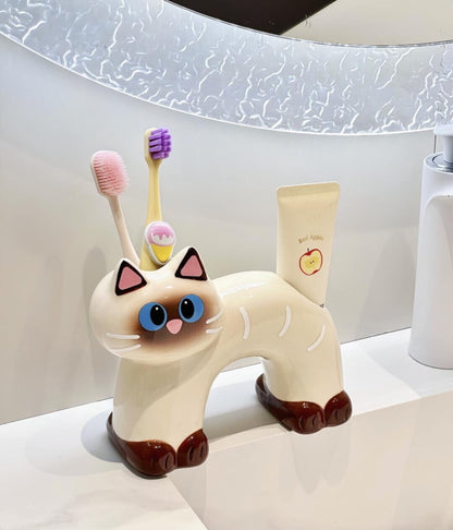 Two ceramic cat toothbrush and toothpaste holders in black and cream, sitting on a neutral tabletop.