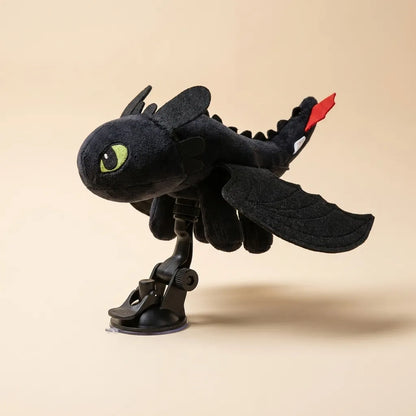 A black plush toy resembling Toothless from How to Your Dragon, mounted on a black suction-cup stand against a solid beige background.