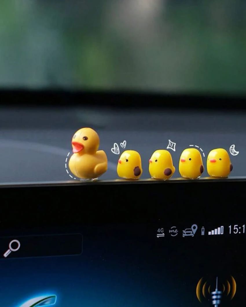 A set of three rubber duck car decorations placed on a vehicle's dashboard, depicting a mother duck and her babies.