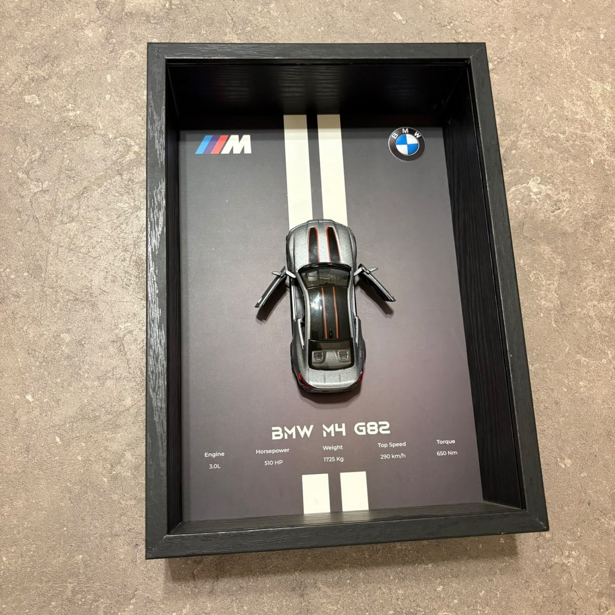 BMW M4 3D Framed Diecast Wall Art in a 32cm x 23cm black shadow box frame, featuring a grey 1:32 scale model car with open doors against an M-Power design background with performance stats.