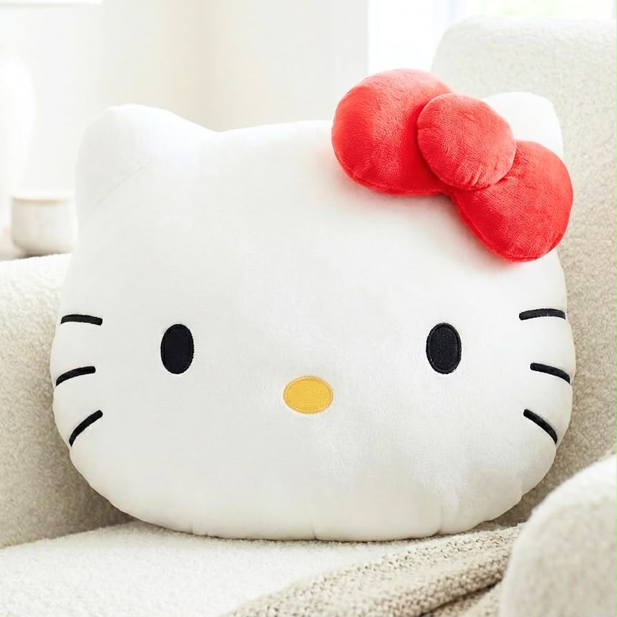Plush toy shaped like a cat face with a red bow on a beige couch.