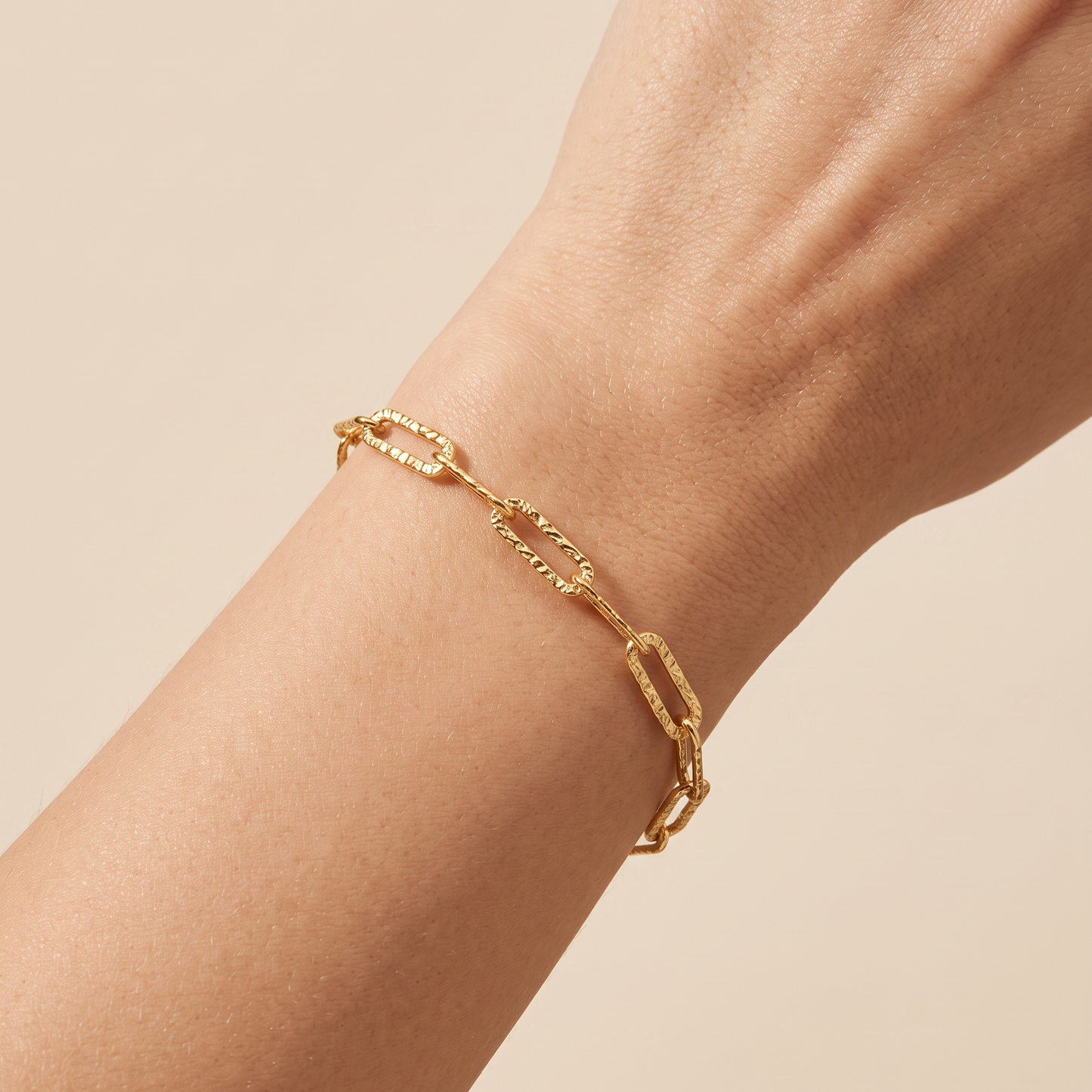 A close-up of a gold chain link bracelet worn on a person's wrist against a soft beige background.