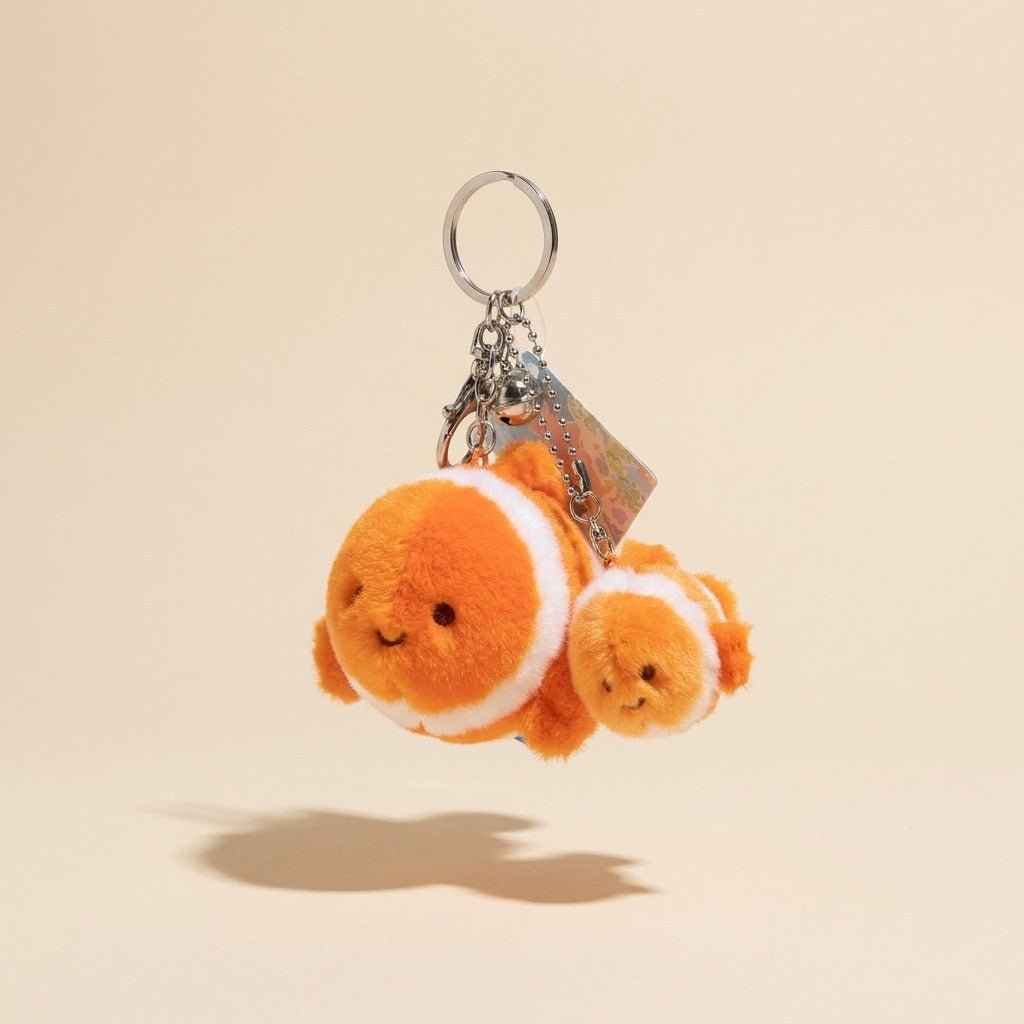 A plush keychain featuring two orange and white clownfish characters with a silver metal key ring and keychain hardware, shown against a solid beige background.